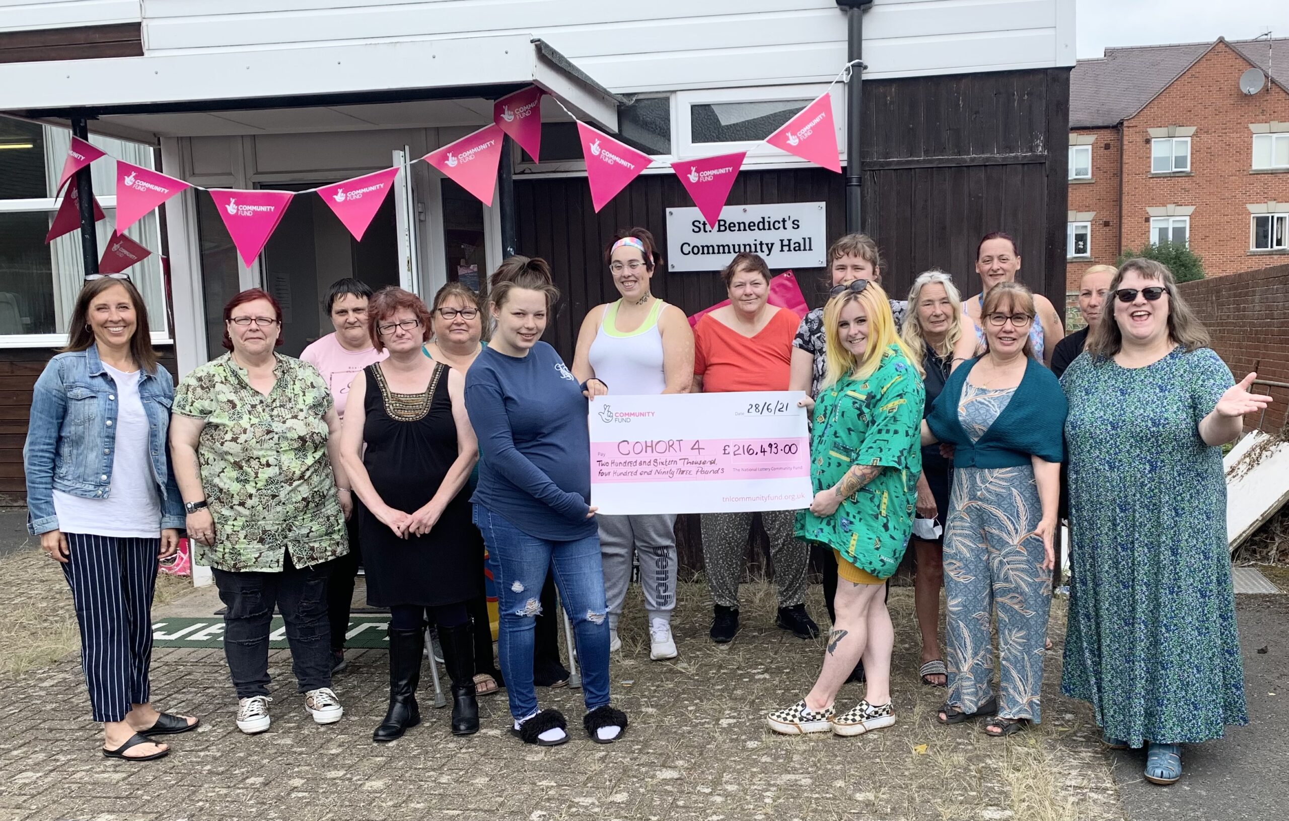 group of women holding up large cheque in front of building